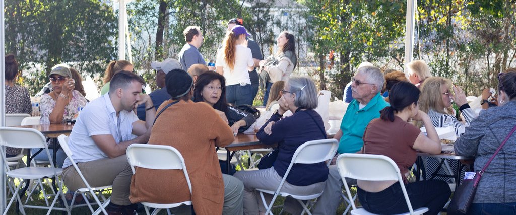 Visitors and parishioners eating at long tables under the tent at the Greek Festival.