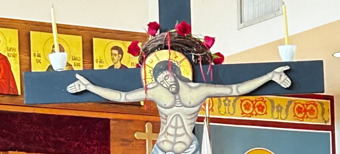 The carved crucifix set up in the church for Holy Week, a crown of thorns and red roses at the head of the cross.