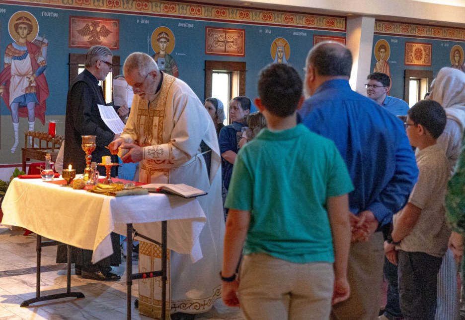 A priest at a candlelit table in the nave during a Holy Week service, with the congregation gathered around.