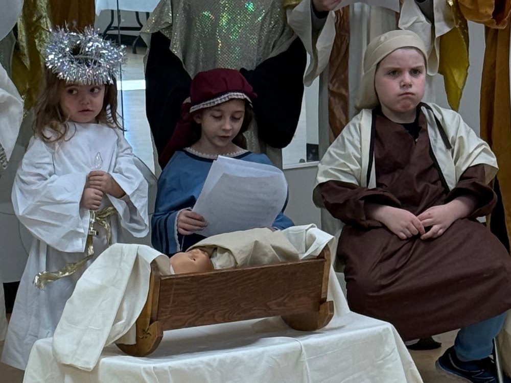 Three children in costume beside the manger during the Sunday School nativity play.