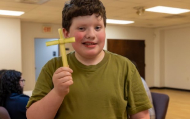 A boy holding up the palm cross he has just folded.