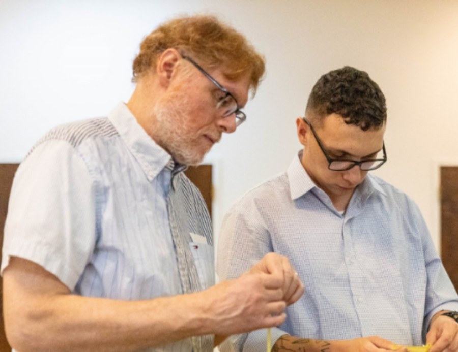 Two parishioners folding palm crosses at a table in the Fellowship Hall.